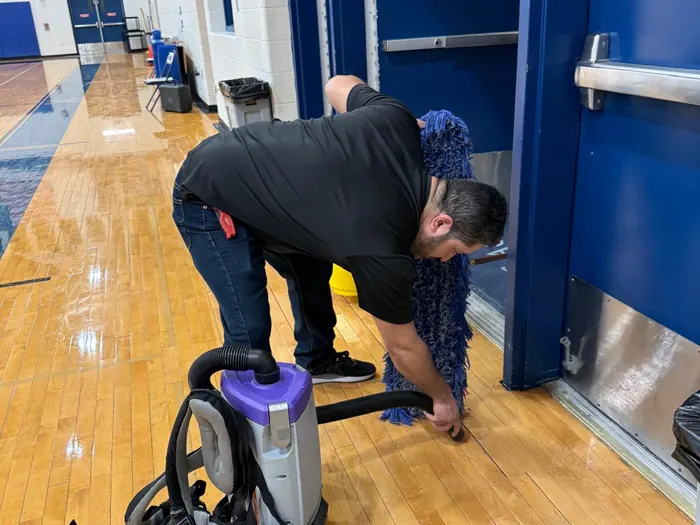 Técnico de Luna Optimum Cleaning usando una aspiradora tipo mochila junto a una puerta azul